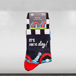 A pair of socks with a race day theme, featuring a car and the text 'IT'S RACE DAY!' on a blue and red design, packaged with a black and white striped card.